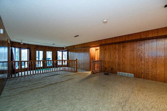 empty room featuring carpet flooring, a textured ceiling, and wooden walls