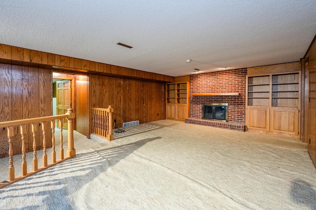 carpeted living room with wooden walls, built in features, a textured ceiling, and a brick fireplace