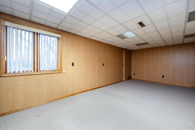 carpeted spare room with a drop ceiling and wooden walls