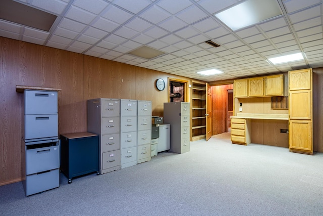 unfurnished office featuring light carpet, a drop ceiling, and wood walls