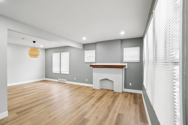 unfurnished living room featuring light hardwood / wood-style floors and a brick fireplace