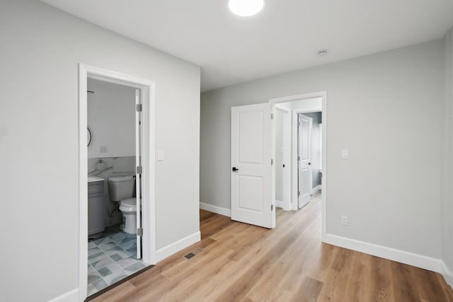 unfurnished bedroom featuring ensuite bath and light wood-type flooring