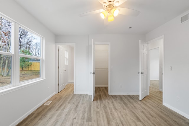 unfurnished bedroom with light wood-type flooring, a walk in closet, visible vents, and baseboards