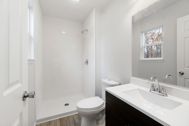 bathroom with a tile shower, vanity, toilet, and wood finished floors