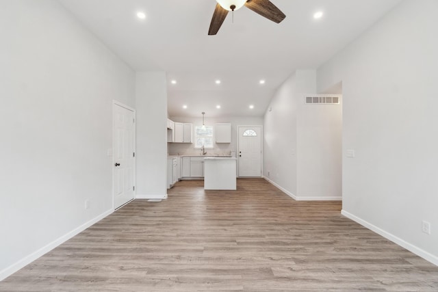 unfurnished living room featuring light wood-style flooring, recessed lighting, a sink, visible vents, and baseboards