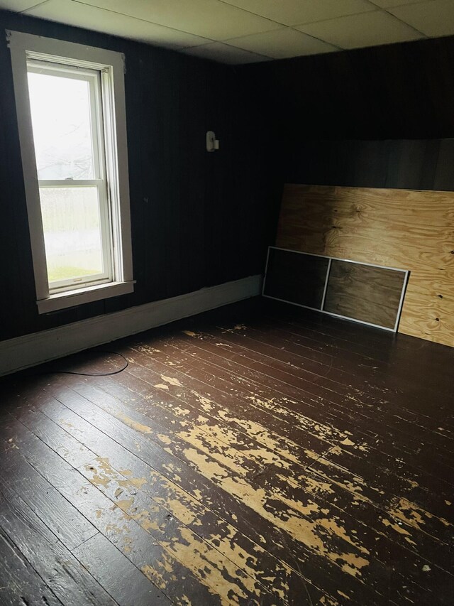 empty room with dark wood-type flooring and a drop ceiling