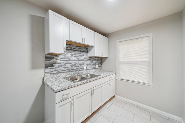 kitchen with decorative backsplash, sink, white cabinets, and light stone countertops