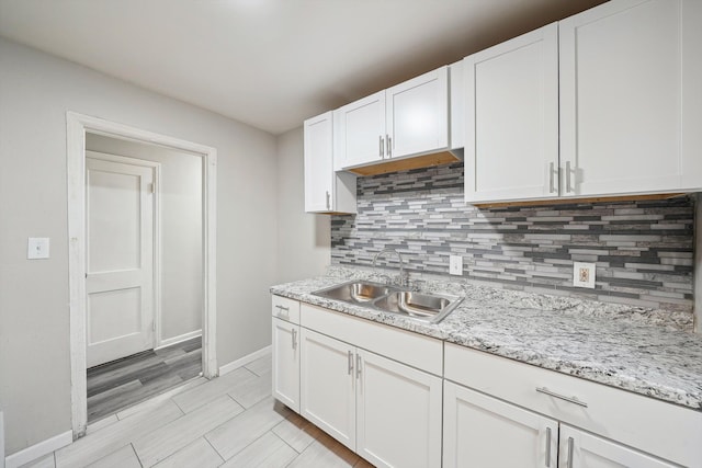 kitchen with tasteful backsplash, light stone countertops, sink, and white cabinets