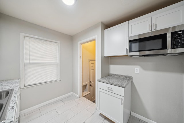 kitchen featuring light stone counters, sink, and white cabinets