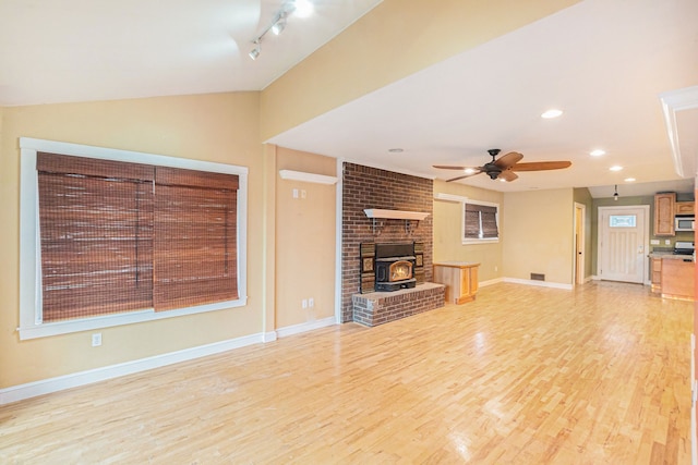 unfurnished living room with ceiling fan, lofted ceiling, light hardwood / wood-style flooring, and a wood stove