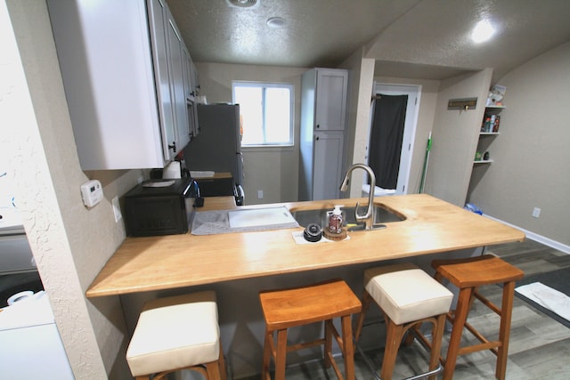 kitchen featuring sink, hardwood / wood-style flooring, fridge, kitchen peninsula, and a breakfast bar area