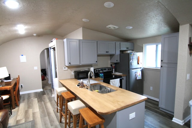 kitchen with black appliances, kitchen peninsula, sink, vaulted ceiling, and wood-type flooring