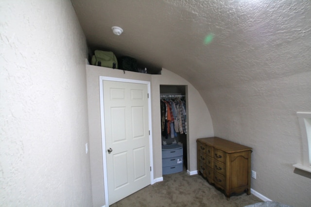 unfurnished bedroom featuring a textured ceiling, a closet, light colored carpet, and vaulted ceiling