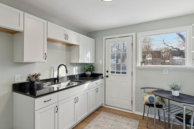 kitchen featuring dark stone countertops, sink, white cabinets, and wood-type flooring