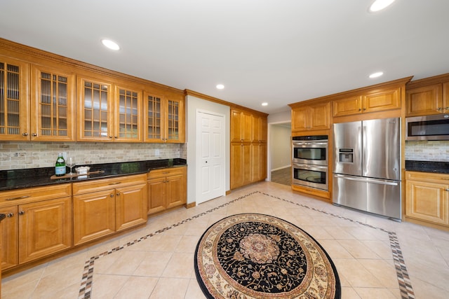 kitchen with crown molding, decorative backsplash, dark stone countertops, light tile patterned flooring, and stainless steel appliances