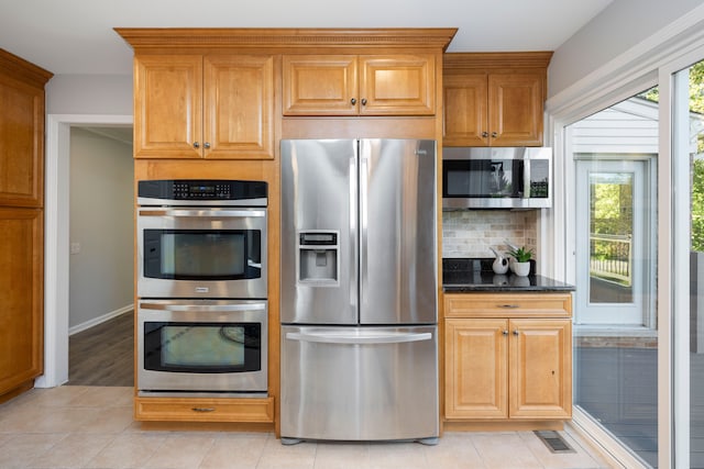 kitchen featuring dark stone counters, decorative backsplash, light tile patterned floors, and stainless steel appliances