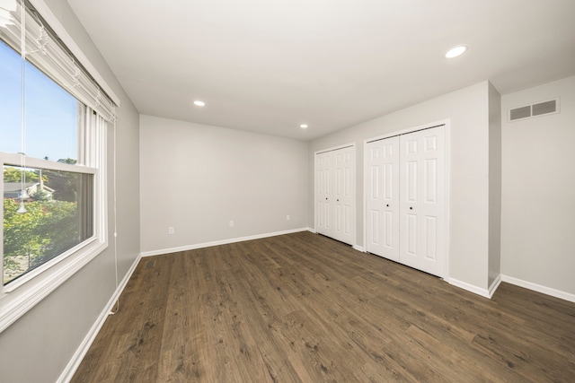 unfurnished bedroom with dark wood-type flooring and multiple closets