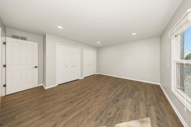 unfurnished bedroom with dark wood-type flooring and two closets