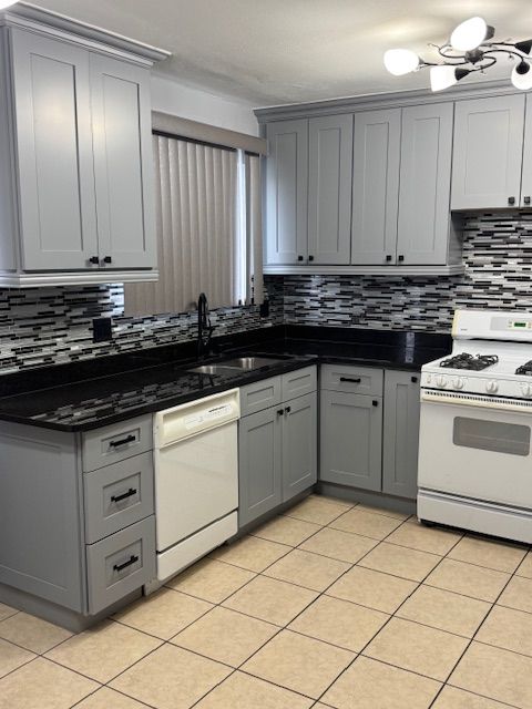 kitchen featuring sink, backsplash, dark stone counters, white appliances, and gray cabinets