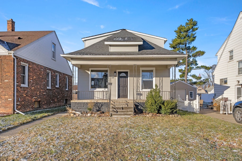 bungalow-style home featuring a front lawn, covered porch, and a storage unit