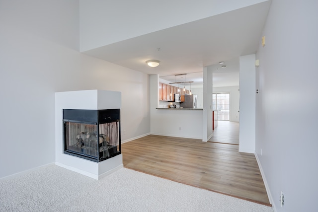 unfurnished living room featuring a multi sided fireplace and light carpet