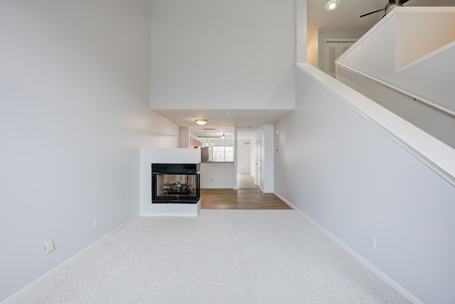 carpeted living room with a multi sided fireplace, a high ceiling, and ceiling fan