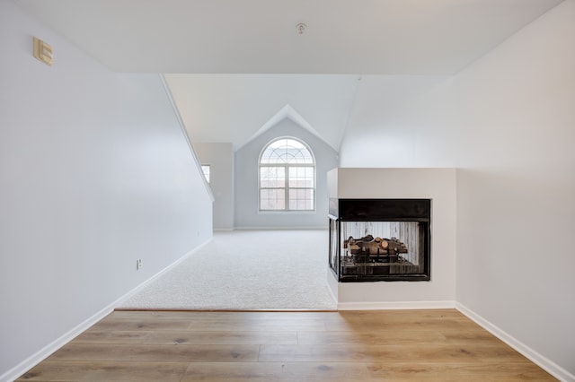 unfurnished living room featuring a multi sided fireplace, light wood-type flooring, and vaulted ceiling