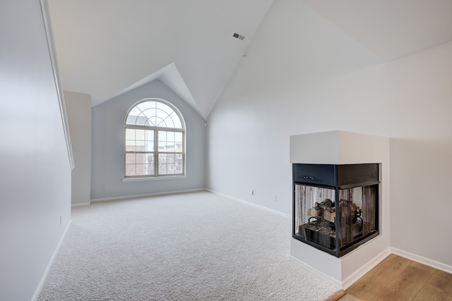 unfurnished living room featuring a multi sided fireplace, light colored carpet, and vaulted ceiling