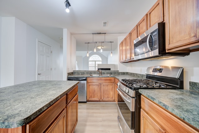 kitchen featuring track lighting, sink, hanging light fixtures, light wood-type flooring, and stainless steel appliances