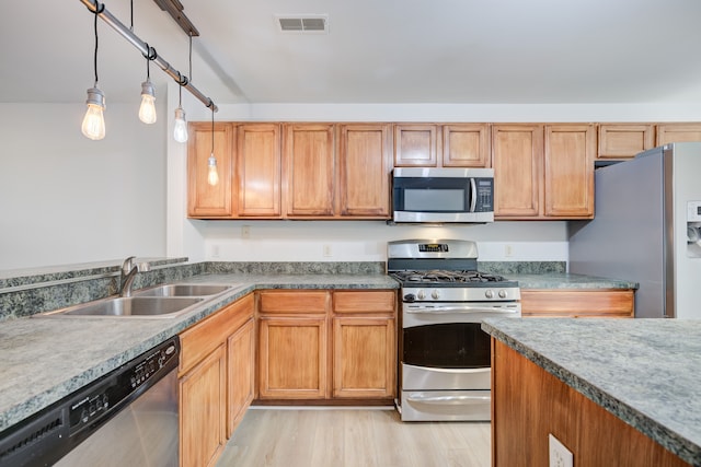 kitchen with hanging light fixtures, sink, stainless steel appliances, and light hardwood / wood-style floors