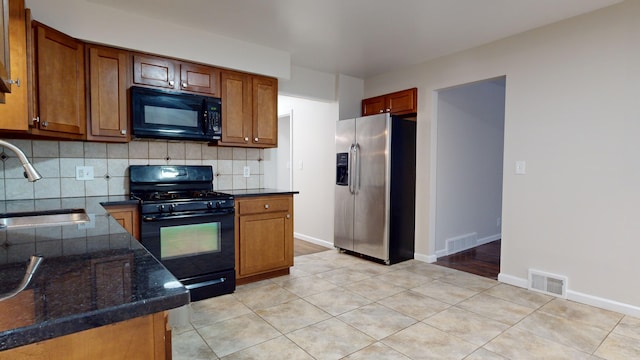 kitchen featuring sink, backsplash, dark stone counters, light tile patterned flooring, and black appliances