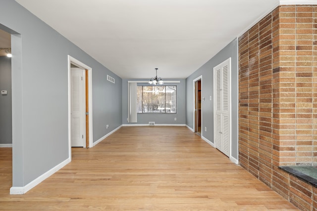 hallway featuring light hardwood / wood-style flooring, brick wall, and an inviting chandelier