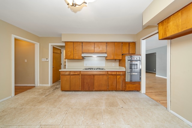 kitchen with cooktop, decorative backsplash, stainless steel double oven, and light hardwood / wood-style floors