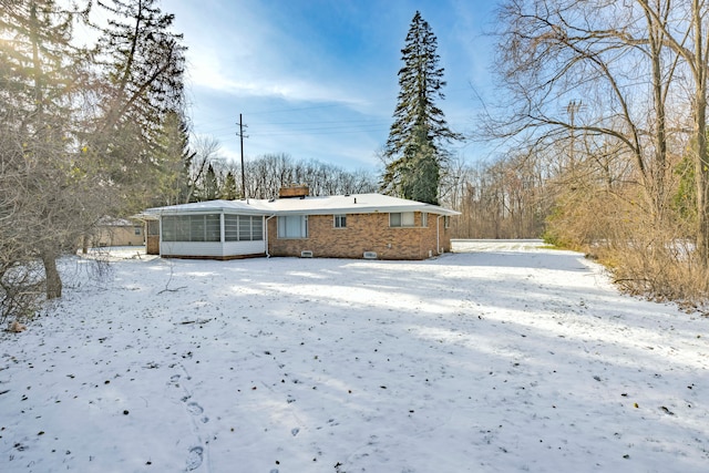 snow covered back of property with a sunroom