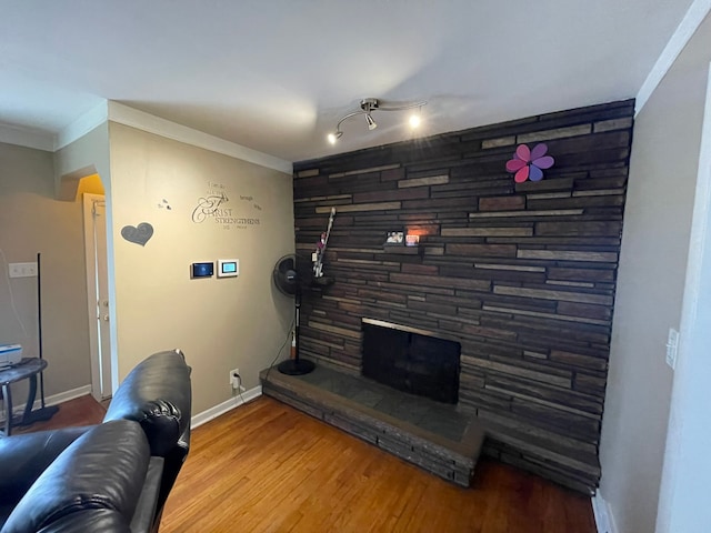 living room with a stone fireplace, crown molding, and wood-type flooring