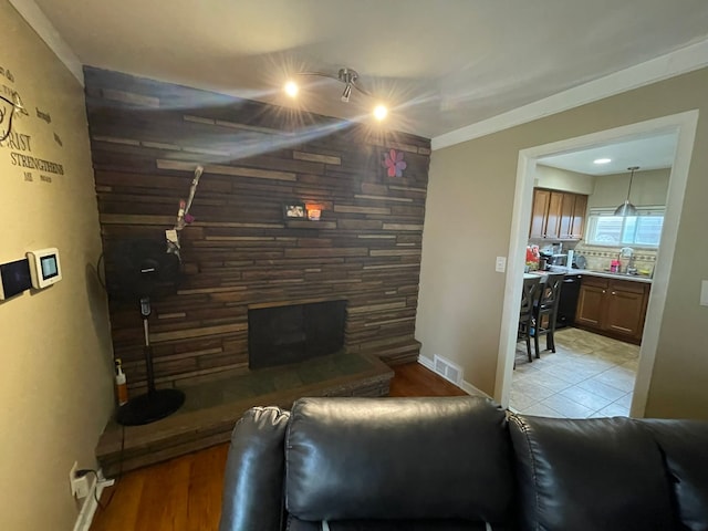 living room featuring light hardwood / wood-style floors, a stone fireplace, crown molding, and sink