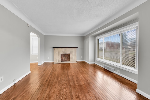 unfurnished living room featuring a textured ceiling, hardwood / wood-style flooring, a wealth of natural light, and a tiled fireplace