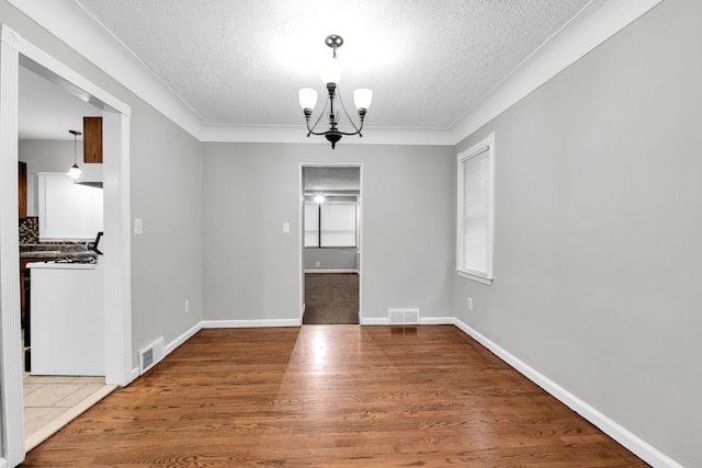 unfurnished dining area with hardwood / wood-style floors, a textured ceiling, and a notable chandelier