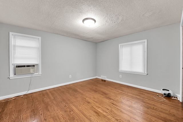 unfurnished room featuring cooling unit, wood-type flooring, and a textured ceiling