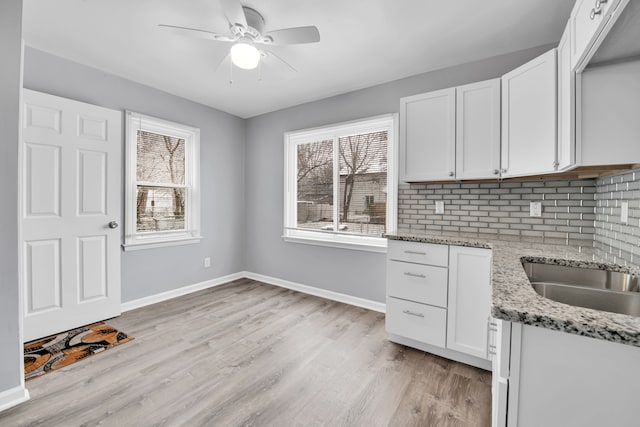 kitchen with light stone countertops, light hardwood / wood-style floors, white cabinetry, and a wealth of natural light