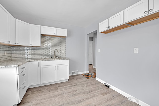 kitchen featuring light stone countertops, white cabinetry, and sink