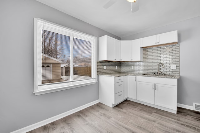 kitchen with light stone counters, sink, white cabinets, and light wood-type flooring