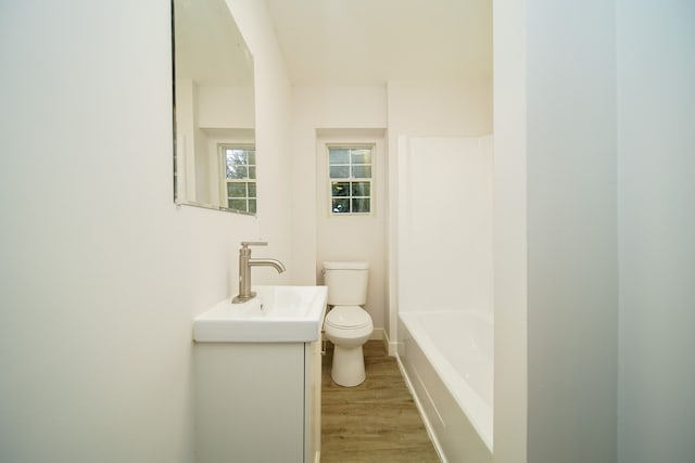 bathroom with a tub, vanity, wood-type flooring, and toilet