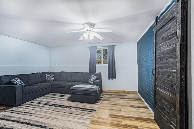 living room with a barn door, wood finished floors, and a ceiling fan