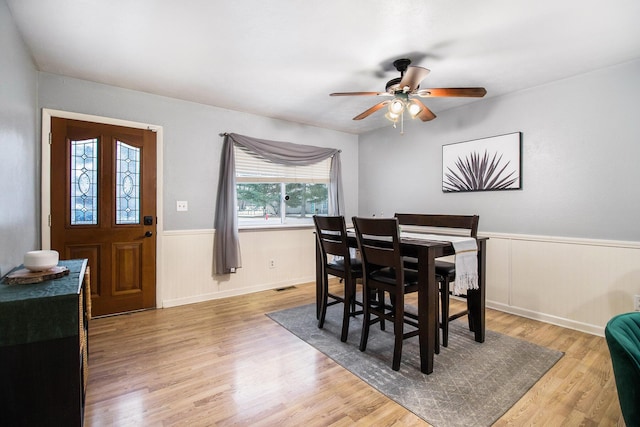 dining space featuring light wood-type flooring, wainscoting, ceiling fan, and visible vents