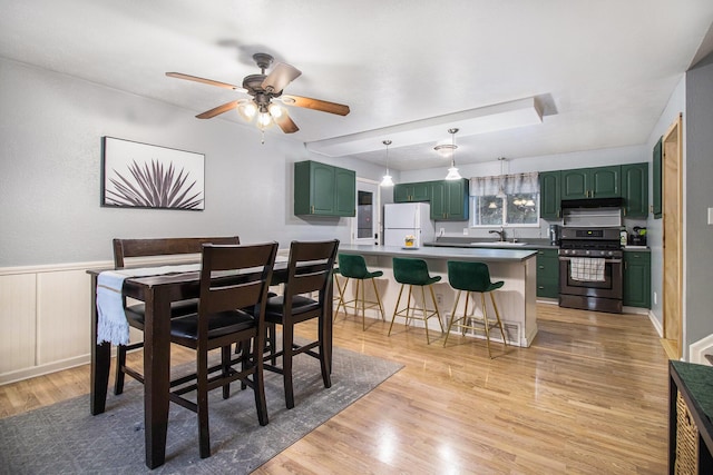 dining space with light wood finished floors, ceiling fan, and a wainscoted wall