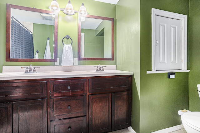 bathroom featuring toilet, double vanity, baseboards, and a sink