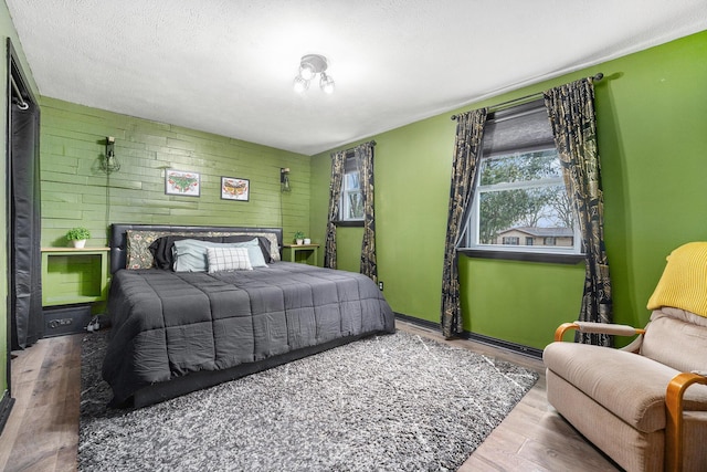 bedroom with a textured ceiling, an accent wall, wood walls, and wood finished floors