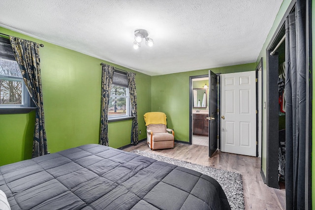 bedroom with connected bathroom, a textured ceiling, baseboards, and wood finished floors