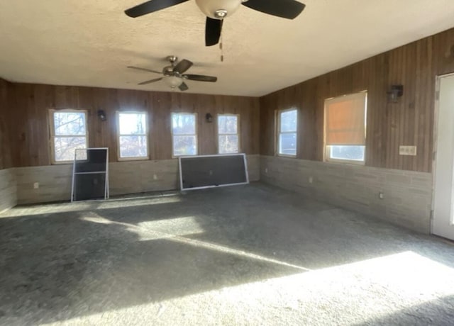 carpeted spare room with a textured ceiling, ceiling fan, and wood walls